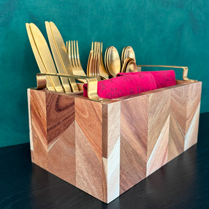 An elegant acacia wood silverware caddy, featuring a beautiful end-grain chevron pattern and matte gold handles, is stylishly filled with gold flatware and a vibrant pink napkin against a dark teal background. An elegant acacia wood silverware caddy, featuring a beautiful end-grain chevron pattern and matte gold handles, is stylishly filled with gold flatware and a vibrant pink napkin against a dark teal background.