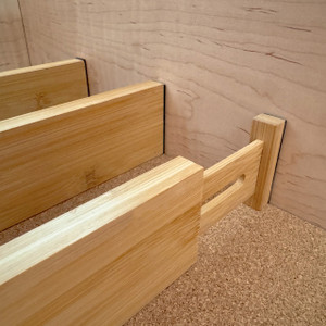 A close-up view of two bamboo drawer dividers installed in an empty drawer, showing the spring-loaded mechanism that expands to create a secure, custom fit for organization.