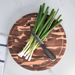 The round end-grain cutting board is shown in a kitchen setting, being used to chop fresh green onions, demonstrating its functionality as a durable prep surface. The round end-grain cutting board is shown in a kitchen setting, being used to chop fresh green onions, demonstrating its functionality as a durable prep surface.