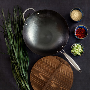 An overhead, styled shot of a black, hammered carbon steel wok and its round wooden lid, elegantly arranged on a dark surface with fresh scallions and small bowls of colorful spices, ready for cooking. An overhead, styled shot of a black, hammered carbon steel wok and its round wooden lid, elegantly arranged on a dark surface with fresh scallions and small bowls of colorful spices, ready for cooking.