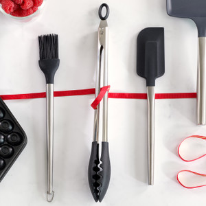 A set of three stainless steel and black silicone kitchen utensils—a basting brush, locking tongs, and a spatula—are elegantly displayed on a white surface, tied with a red ribbon, suggesting a perfect gift set. A set of three stainless steel and black silicone kitchen utensils—a basting brush, locking tongs, and a spatula—are elegantly displayed on a white surface, tied with a red ribbon, suggesting a perfect gift set.