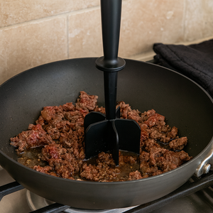 A black, heat-resistant nylon meat chopper is shown in a non-stick pan, easily breaking up and crumbling ground meat as it cooks on a stovetop. A black, heat-resistant nylon meat chopper is shown in a non-stick pan, easily breaking up and crumbling ground meat as it cooks on a stovetop.