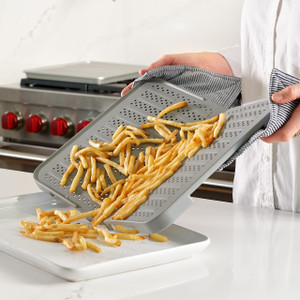 A person uses the gray folding baking mat to easily pour crispy, golden french fries from the mat onto a serving platter. A person uses the gray folding baking mat to easily pour crispy, golden french fries from the mat onto a serving platter.