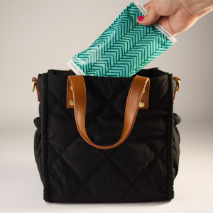 A hand places a reusable, patterned ice pack into a black quilted tote bag to keep its contents cool. A hand places a reusable, patterned ice pack into a black quilted tote bag to keep its contents cool.