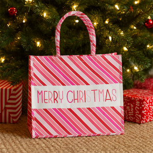 “Merry Christmas” XL canvas tote with red, pink, and white candy-cane stripes under a lit Christmas tree “Merry Christmas” XL canvas tote with red, pink, and white candy-cane stripes under a lit Christmas tree