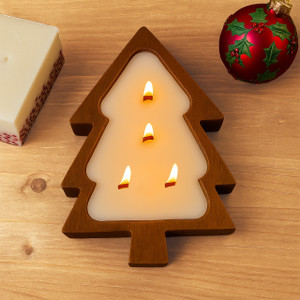 A beautiful Tree Shaped Wood Candle, crafted from Paulownia wood, is shown with its four wood wicks lit and glowing warmly, creating a cozy holiday centerpiece on a wooden table next to a festive ornament.