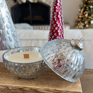 A beautiful Silver Bell Ornament Candle made of ridged, silver mercury glass is displayed open on a wooden mantel, revealing the wood wick candle inside, with a cozy fireplace and Christmas tree in the background. A beautiful Silver Bell Ornament Candle made of ridged, silver mercury glass is displayed open on a wooden mantel, revealing the wood wick candle inside, with a cozy fireplace and Christmas tree in the background.