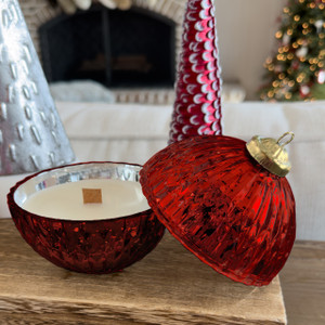 A beautiful Red Bell Ornament Candle made of ridged, red mercury glass is displayed open on a wooden mantel, revealing the wood wick candle inside, with a cozy fireplace and Christmas tree in the background. A beautiful Red Bell Ornament Candle made of ridged, red mercury glass is displayed open on a wooden mantel, revealing the wood wick candle inside, with a cozy fireplace and Christmas tree in the background.