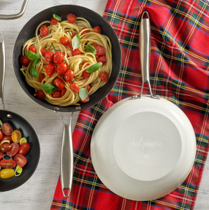Overhead of two Bel Piatto No.10 cast iron fry pans—one filled with cherry-tomato pasta, the other flipped to show the glossy white enameled exterior and stainless handle on a plaid towel Overhead of two Bel Piatto No.10 cast iron fry pans—one filled with cherry-tomato pasta, the other flipped to show the glossy white enameled exterior and stainless handle on a plaid towel
