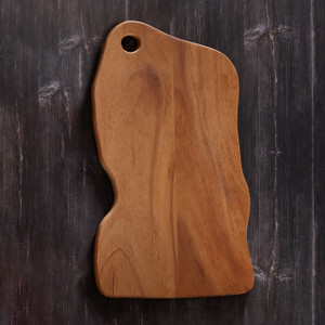 A natural edge walnut wood cutting board with a unique organic shape and a finger grip cutout, displayed on a dark, textured background. A natural edge walnut wood cutting board with a unique organic shape and a finger grip cutout, displayed on a dark, textured background.