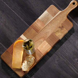 An Acacia Mosaic Paddle Board featuring a mosaic pattern of wood pieces, displayed with cheese, crackers, and pickles on a dark wooden surface. The board has an extended handle. An Acacia Mosaic Paddle Board featuring a mosaic pattern of wood pieces, displayed with cheese, crackers, and pickles on a dark wooden surface. The board has an extended handle.