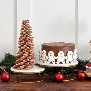 Two white marble pedestal stands with gold bases styled for the holidays—one holding a chocolate cake, one a cookie tree Two white marble pedestal stands with gold bases styled for the holidays—one holding a chocolate cake, one a cookie tree