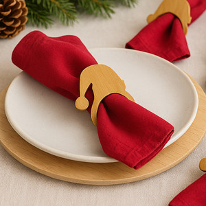 Red linen napkin on a white plate, held by a wooden Santa hat napkin ring, with holiday greenery and decor softly blurred in the background.