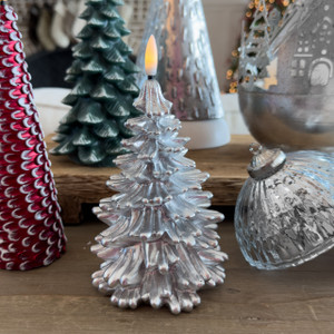 A Silver Christmas Tree Flameless Candle, crafted from shimmery metallic silver paraffin wax, is glowing warmly as part of a sophisticated holiday tabletop display with other festive decor. A Silver Christmas Tree Flameless Candle, crafted from shimmery metallic silver paraffin wax, is glowing warmly as part of a sophisticated holiday tabletop display with other festive decor.