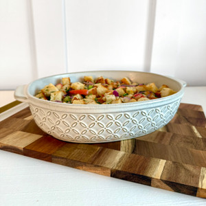 Embossed oval stoneware baker in matte biscuit finish filled with casserole on a wooden board, showing flutter pattern and side handles Embossed oval stoneware baker in matte biscuit finish filled with casserole on a wooden board, showing flutter pattern and side handles