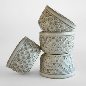 Embossed stoneware ramekins in matte biscuit finish, three stacked with a fourth leaning, showing scalloped pin-dot design Embossed stoneware ramekins in matte biscuit finish, three stacked with a fourth leaning, showing scalloped pin-dot design