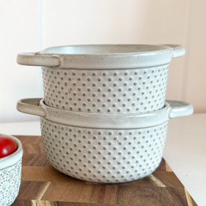 Stack of two biscuit-colored embossed stoneware soup bowls with handles on a wooden board