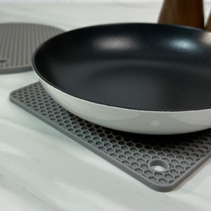 Nonstick frying pan resting on a gray honeycomb-pattern silicone hot pad on a countertop