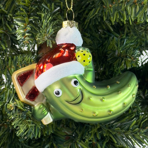 Pickleball Santa glass ornament hanging on a Christmas tree—smiling pickle in a Santa hat holding a paddle and pickleball Pickleball Santa glass ornament hanging on a Christmas tree—smiling pickle in a Santa hat holding a paddle and pickleball