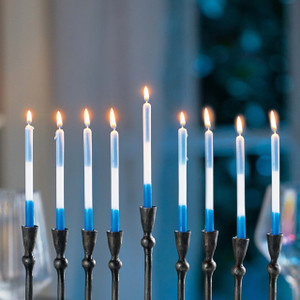 A set of beautiful blue and white Menorah Taper Candles are lit and glowing warmly in a dark metal menorah, celebrating the festival of lights during Hanukkah.