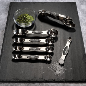 Stainless magnetic measuring spoons laid out on a slate board; double-sided spoons with printed sizes and a nested stack