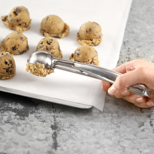Hand using a stainless steel spring-release cookie scoop to portion dough onto a parchment-lined baking sheet