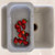 A gray, expandable strainer is shown extended over a white kitchen sink, filled with freshly washed red strawberries, demonstrating its over-the-sink functionality for rinsing produce.