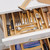 A top-down view of a bamboo bag organizer placed inside a kitchen drawer, with its four compartments neatly filled with gallon, quart, sandwich, and snack-sized plastic storage bags.