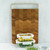 A rectangular acacia wood board with a striking end-grain chevron pattern and a modern matte gold handle is displayed vertically in a kitchen, with glass meal prep containers in front of it.