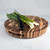 A beautiful Acacia Round End Grain Board is displayed on a white marble countertop, holding a fresh bunch of green onions and a small paring knife, ready for vegetable prep.