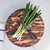 The round end-grain cutting board is shown in a kitchen setting, being used to chop fresh green onions, demonstrating its functionality as a durable prep surface.