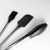 A stylized, black and white photo showcasing the complete three-piece utensil set, including the basting brush, spatula, and locking tongs, arranged together to highlight their matching design.