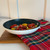 An 8-inch cast iron fry pan with a nonstick ceramic interior, containing sautéed cherry tomatoes and leeks,. The pan has a stainless steel handle and is placed on a white surface with a plaid cloth.