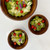 Three acacia wood bowls of various sizes arranged on a white surface, with two bowls containing salad and one empty, showcasing a potential serving set.