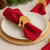 Red linen napkin on a white plate, held by a wooden Santa hat napkin ring, with holiday greenery and decor softly blurred in the background.