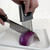 Hand using a stainless steel slicing holder to guide a chef’s knife while cutting a red onion on a cutting board