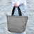 A person is holding the expanded lava gray Navigator Tote by its black handles, showcasing its full size and lightweight design.