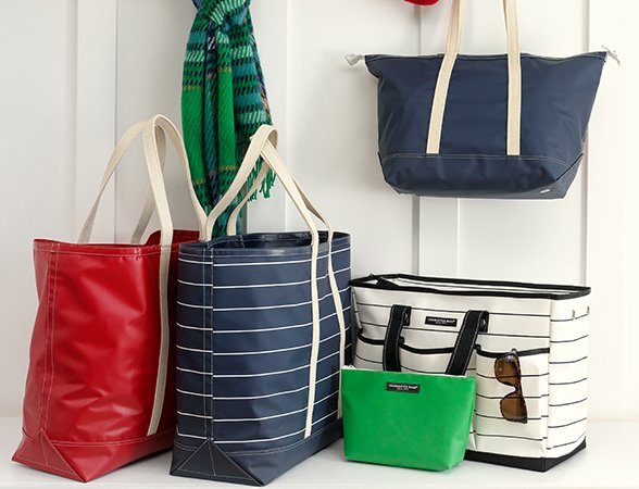 Striped and solid Charleston Bags™ displayed with a scarf and sunglasses on wall hooks