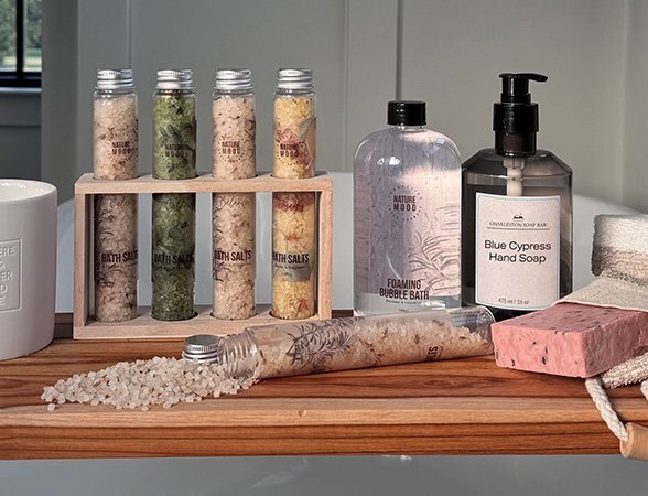 Spa gifts displayed on a wooden bath tray, including bath salts, bubble bath, soap, and hand wash