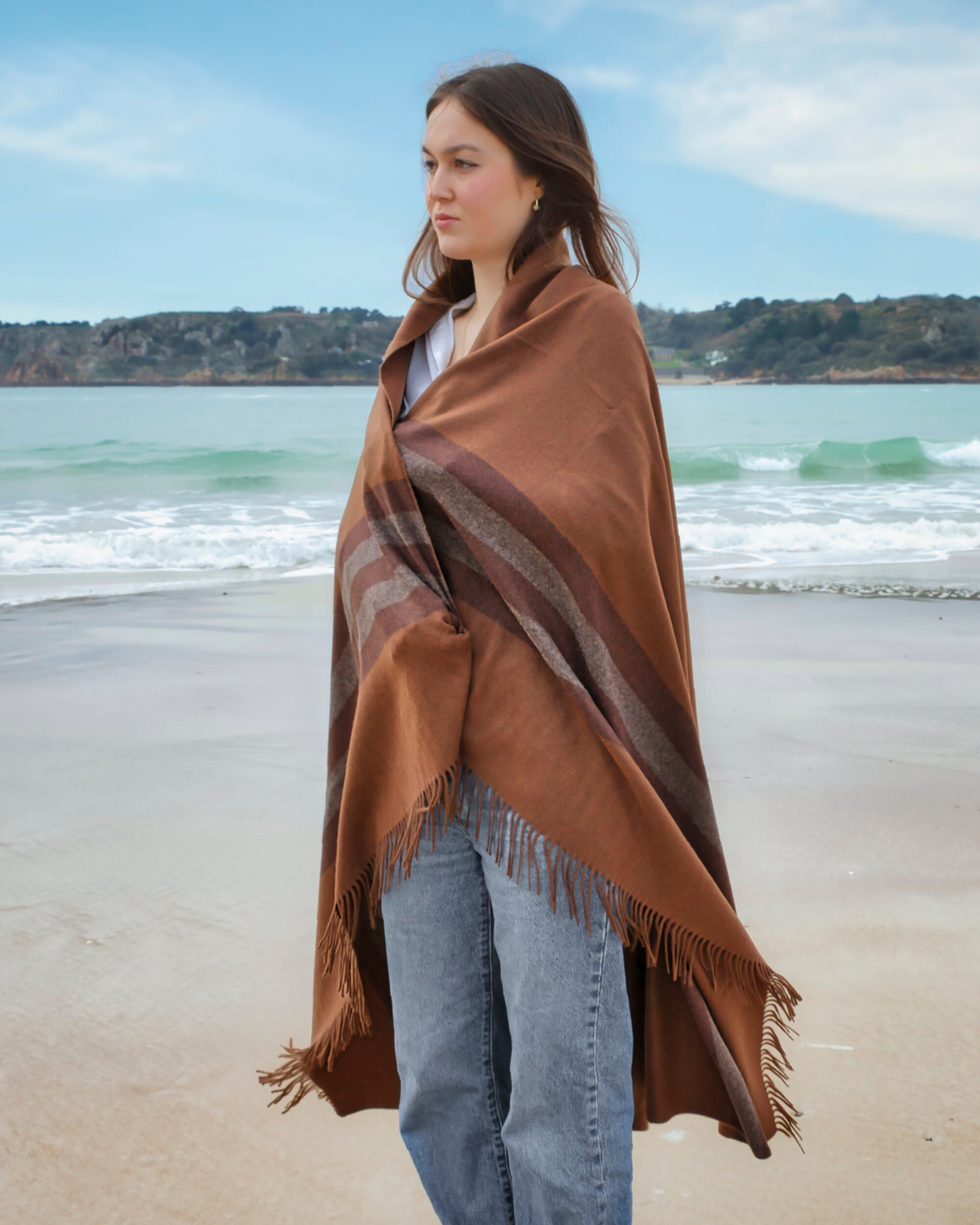 Model on beach wearing brown cashmere striped blanket with tassels