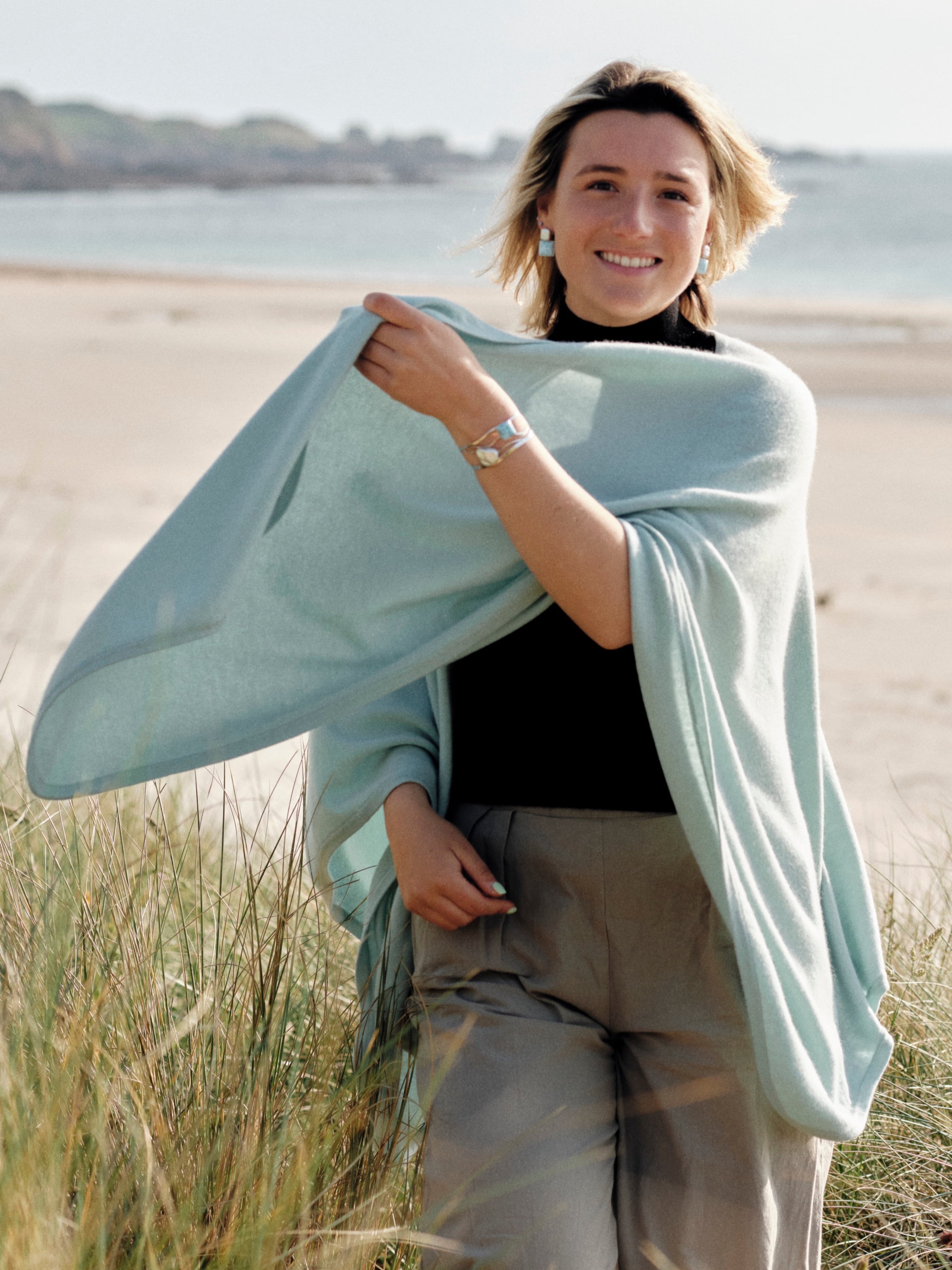 Model outdoors wearing a mint green cashmere cape with elegant draping