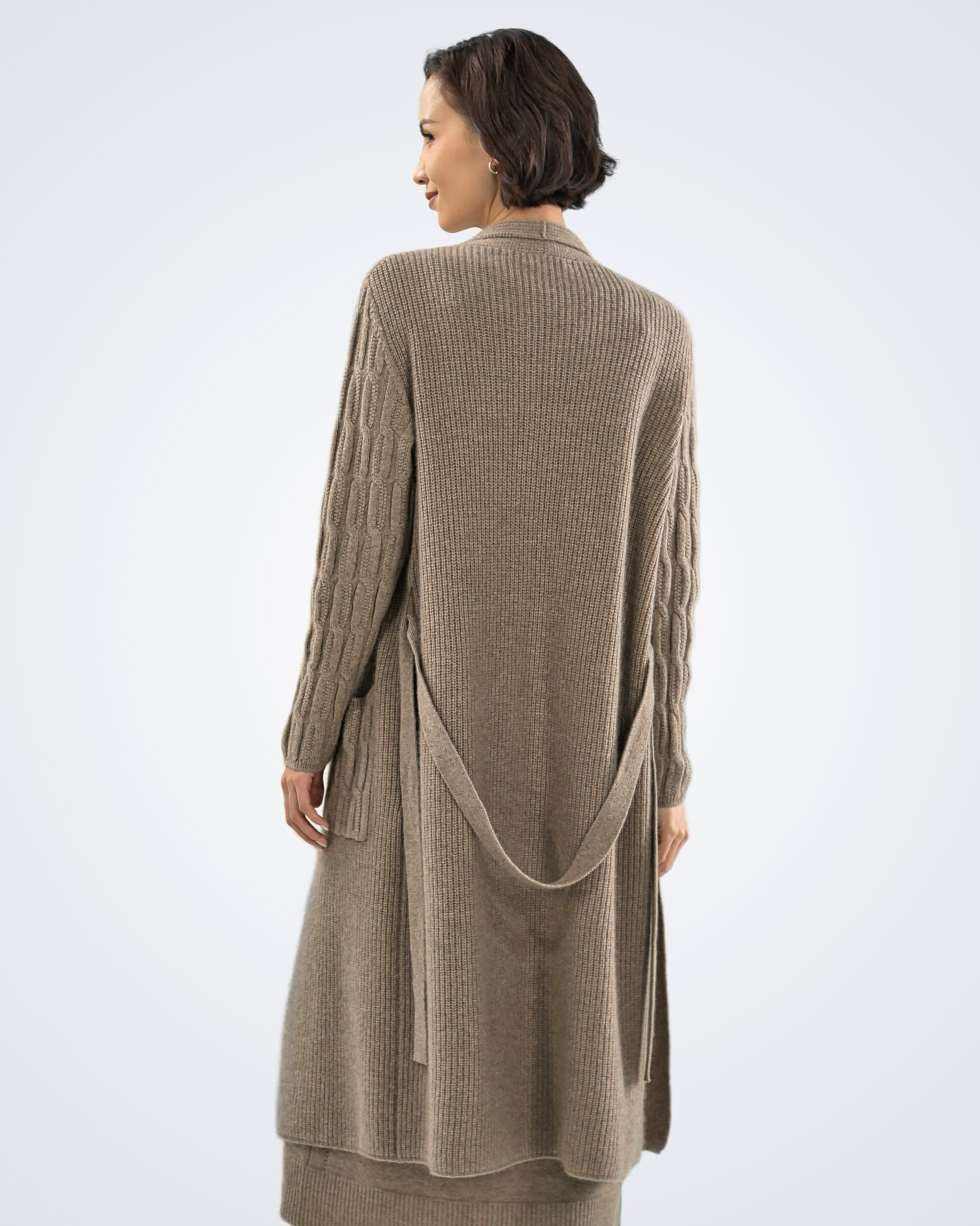 Unur model wearing a natural brown ribbed cashmere long cardigan with cable detail, rear view