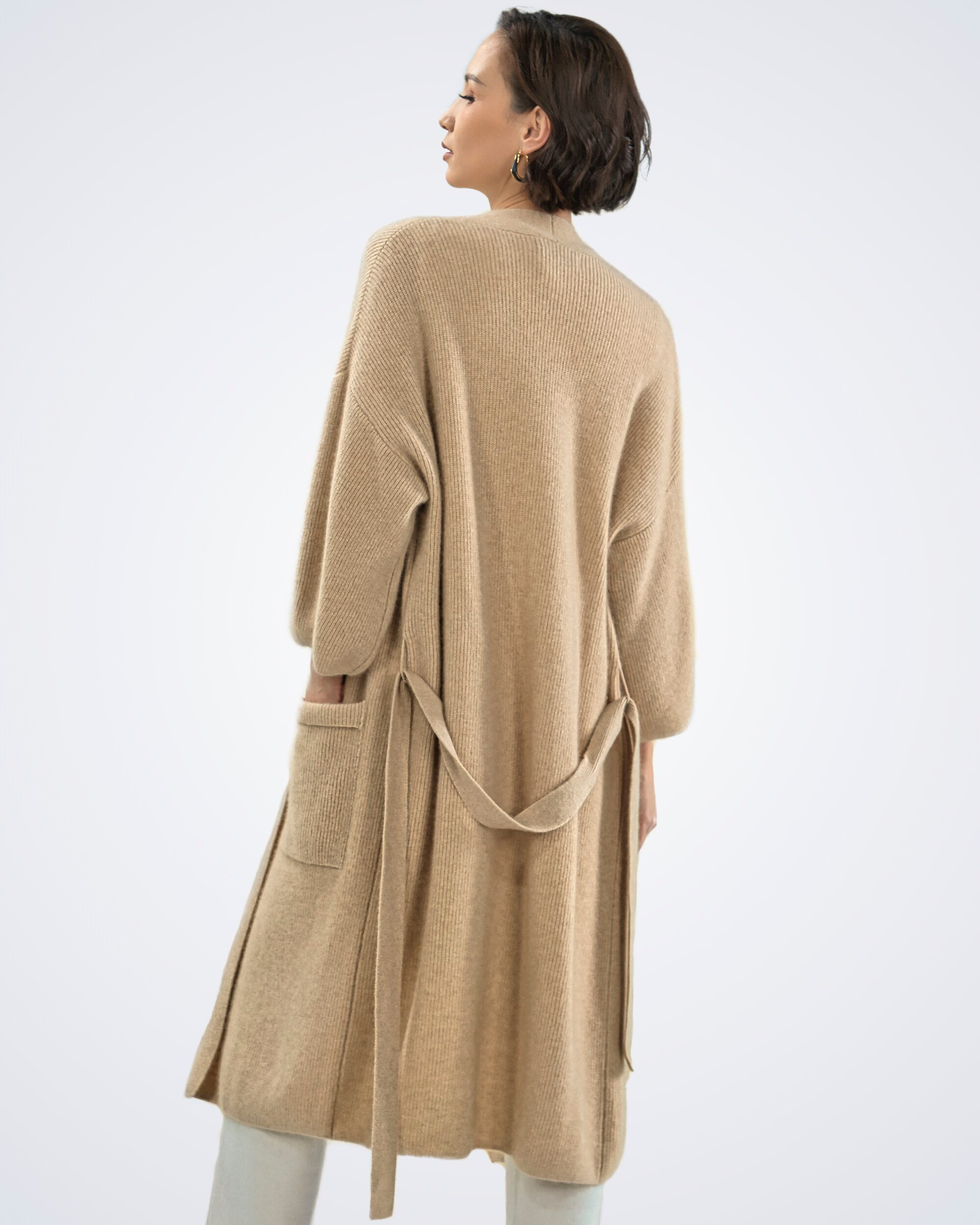 Unur model wearing a natural beige ribbed cashmere long cardigan coat with a tie belt, rear view