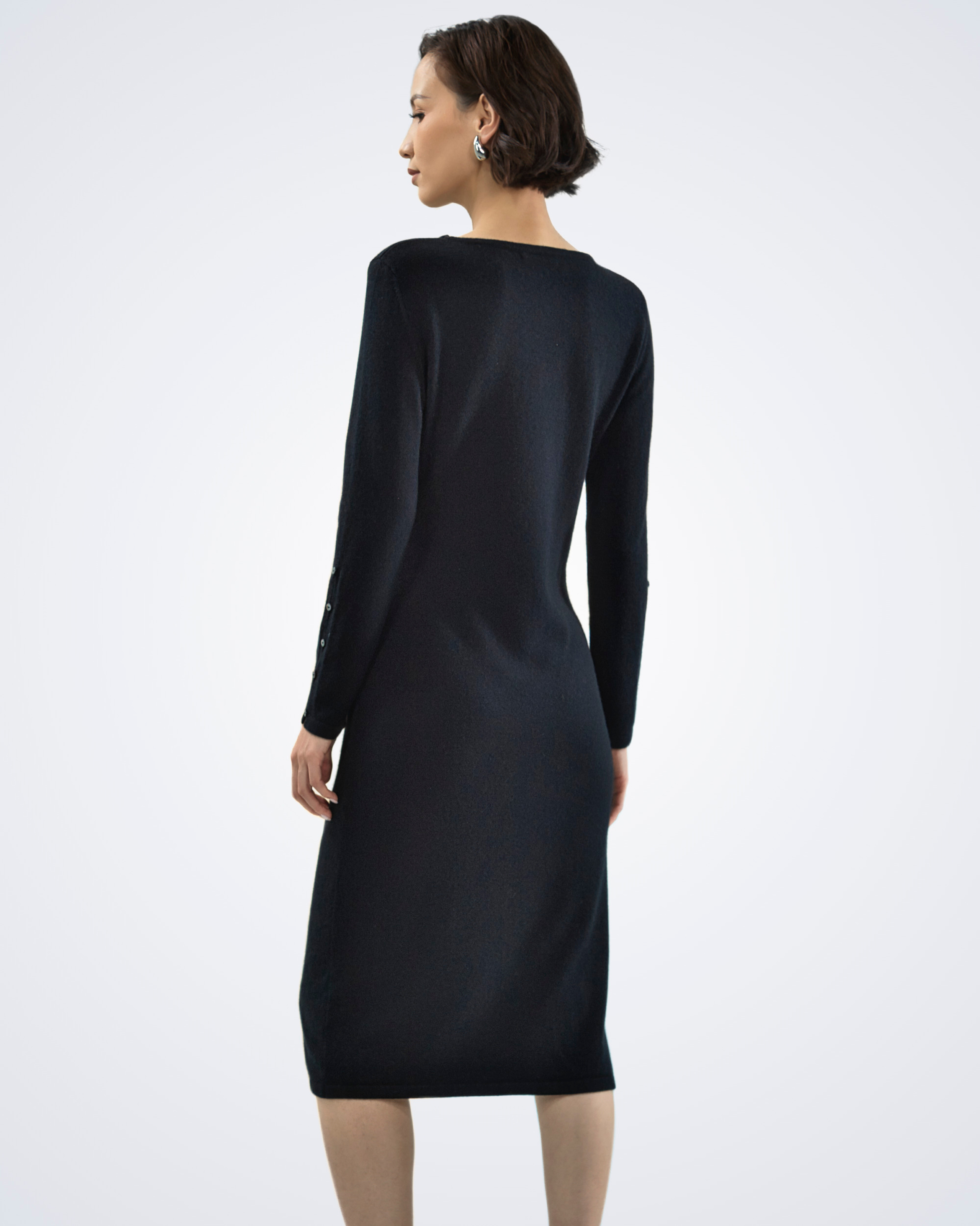 Unur model wearing a black cashmere midi dress with buttoned sleeves and a boat neckline, rear view