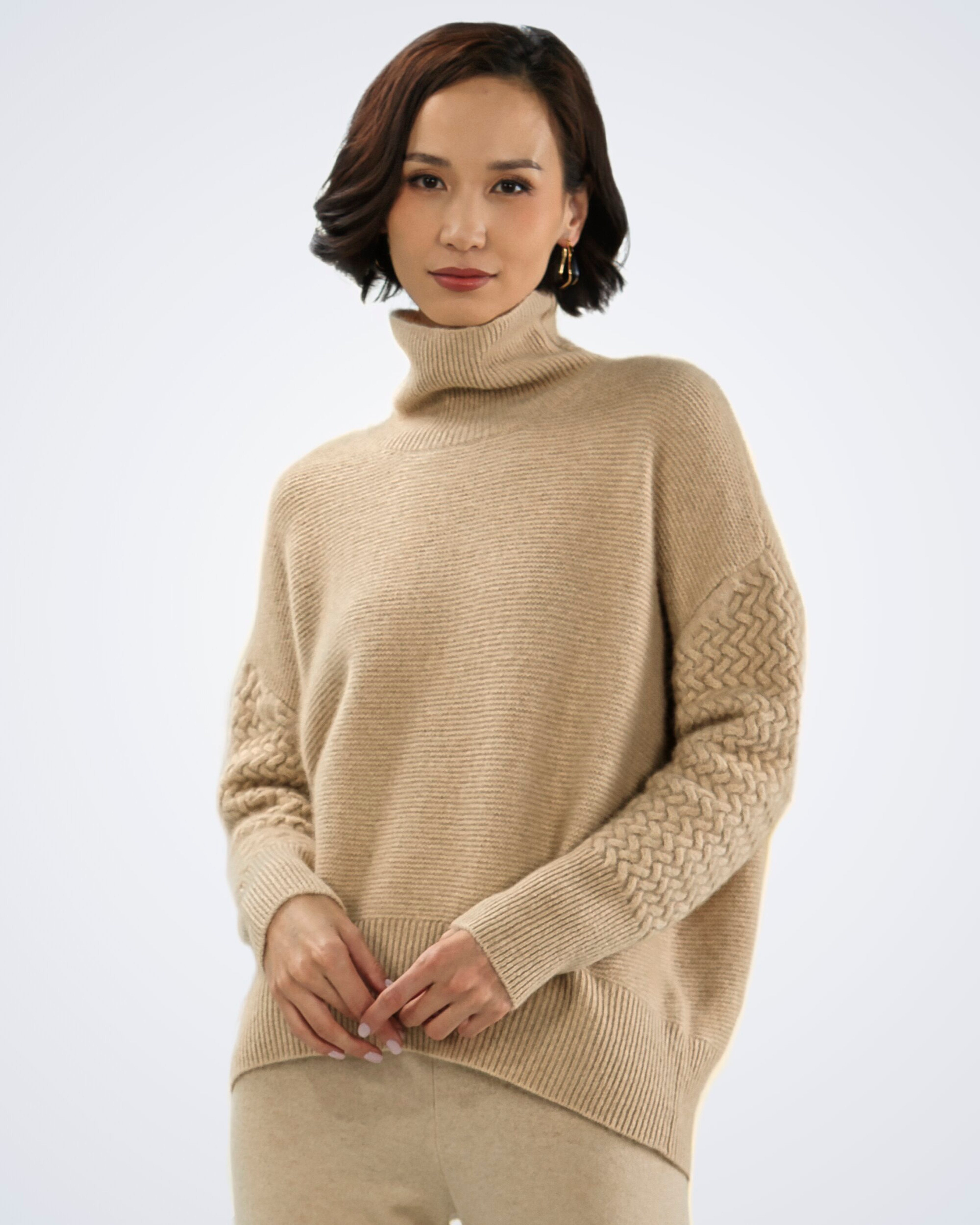 Unur model wearing an oversized natural beige cashmere jumper with cable-knit sleeves and a roll neck