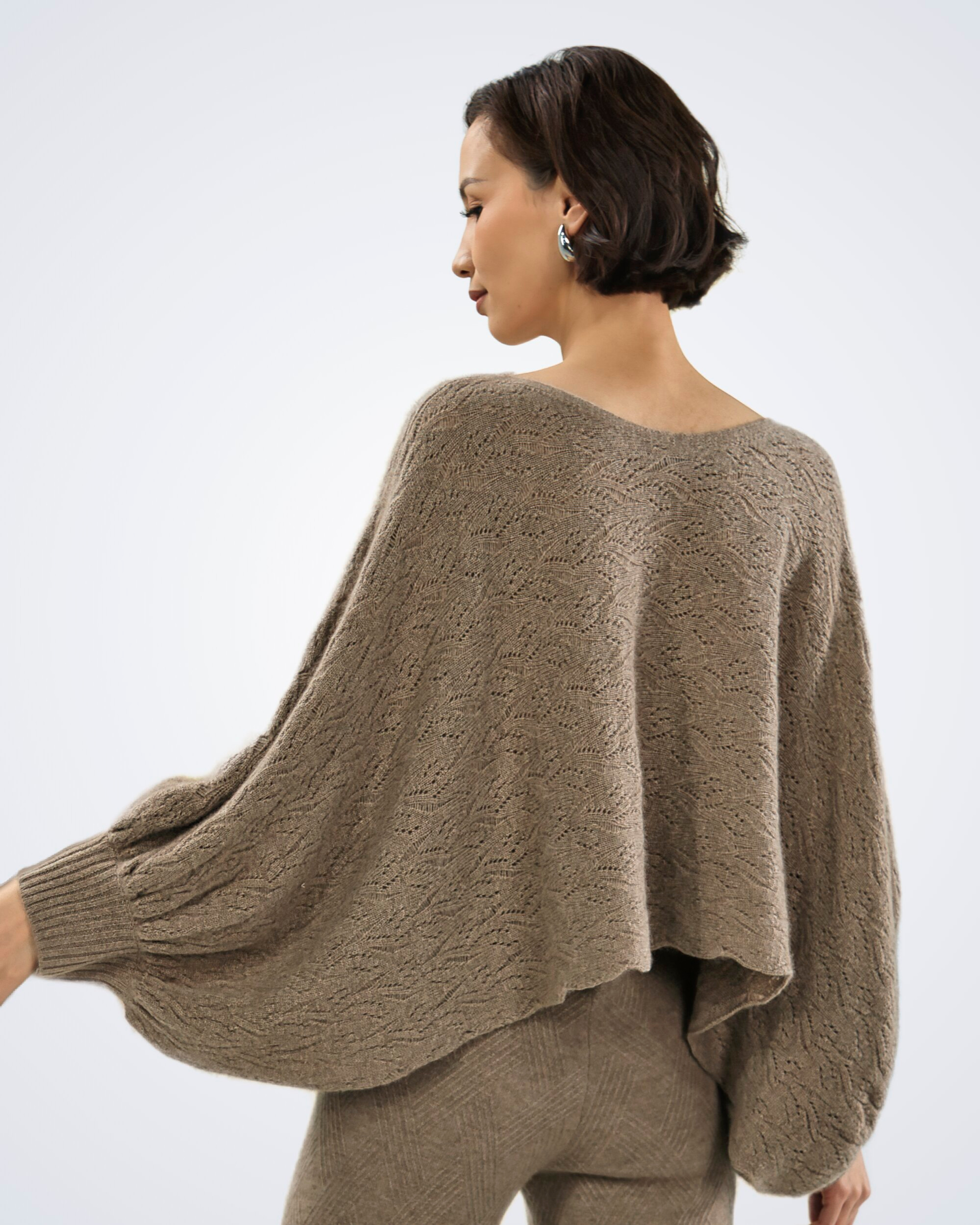 Unur model wearing a natural brown patterned loose-knit cashmere poncho-style jumper, back view