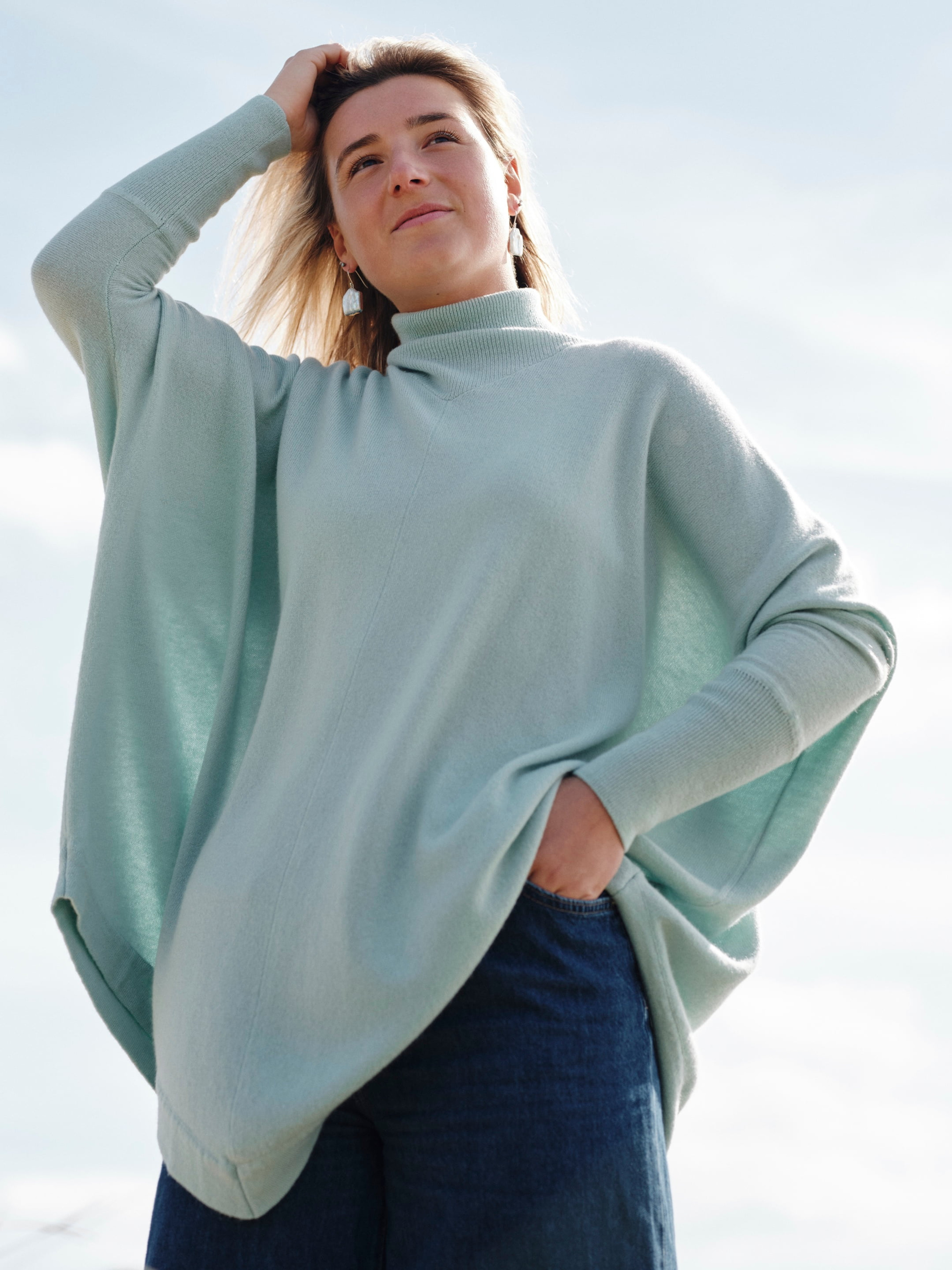 Model outdoors wearing a mint green batwing turtleneck cashmere poncho with ribbing