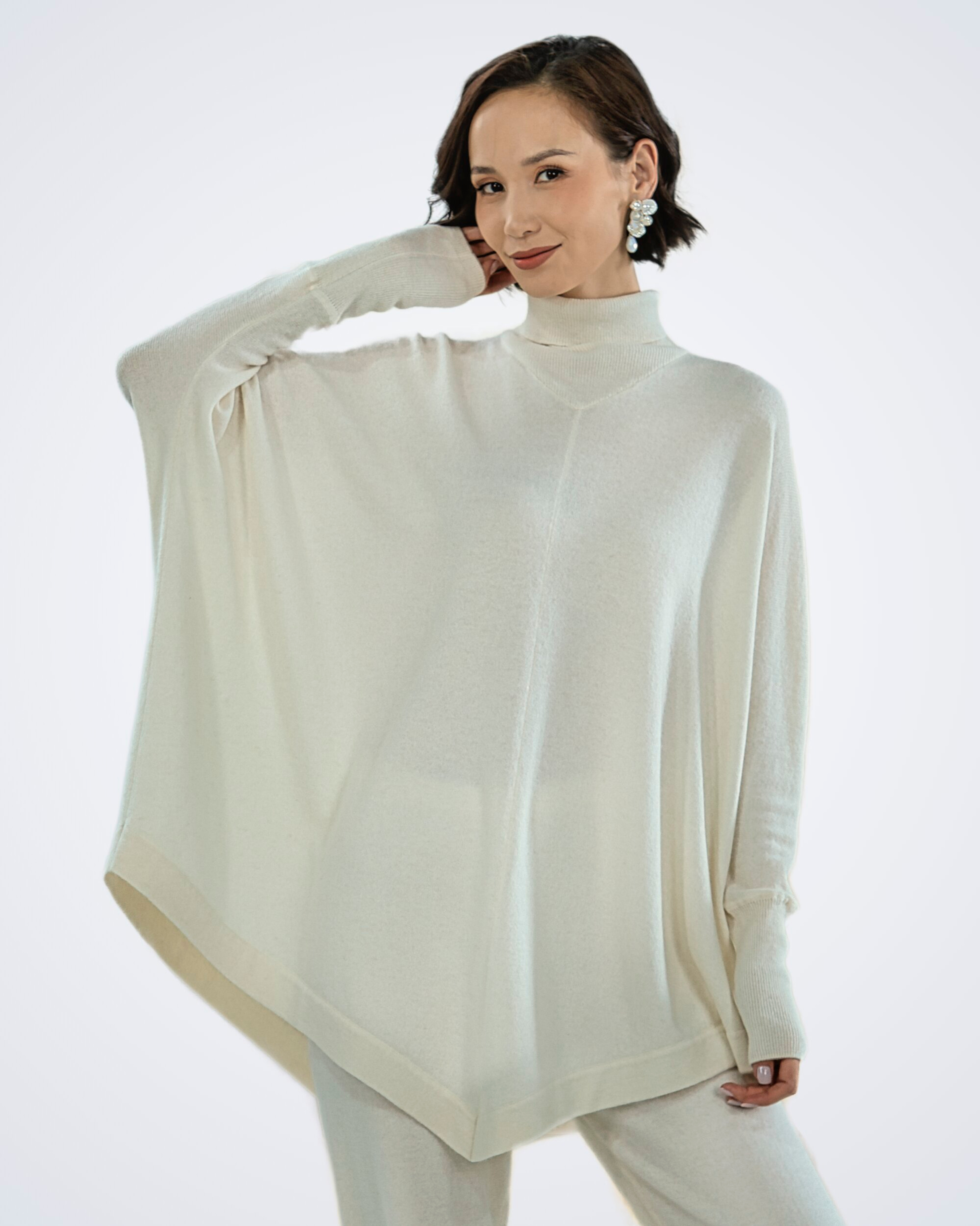 Unur model wearing a white batwing turtleneck cashmere poncho with ribbing