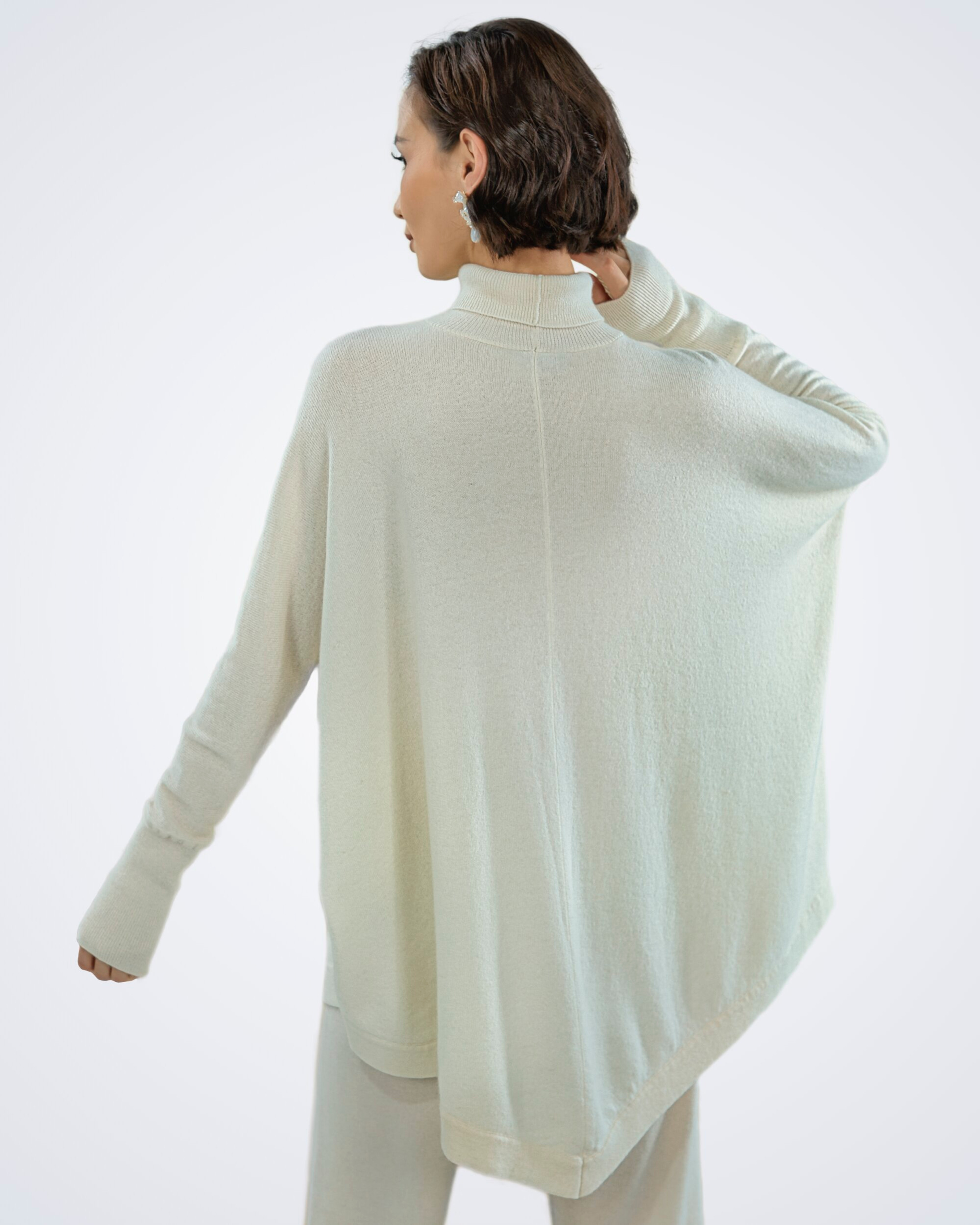 Unur model wearing a white batwing turtleneck cashmere poncho with ribbing, rear view