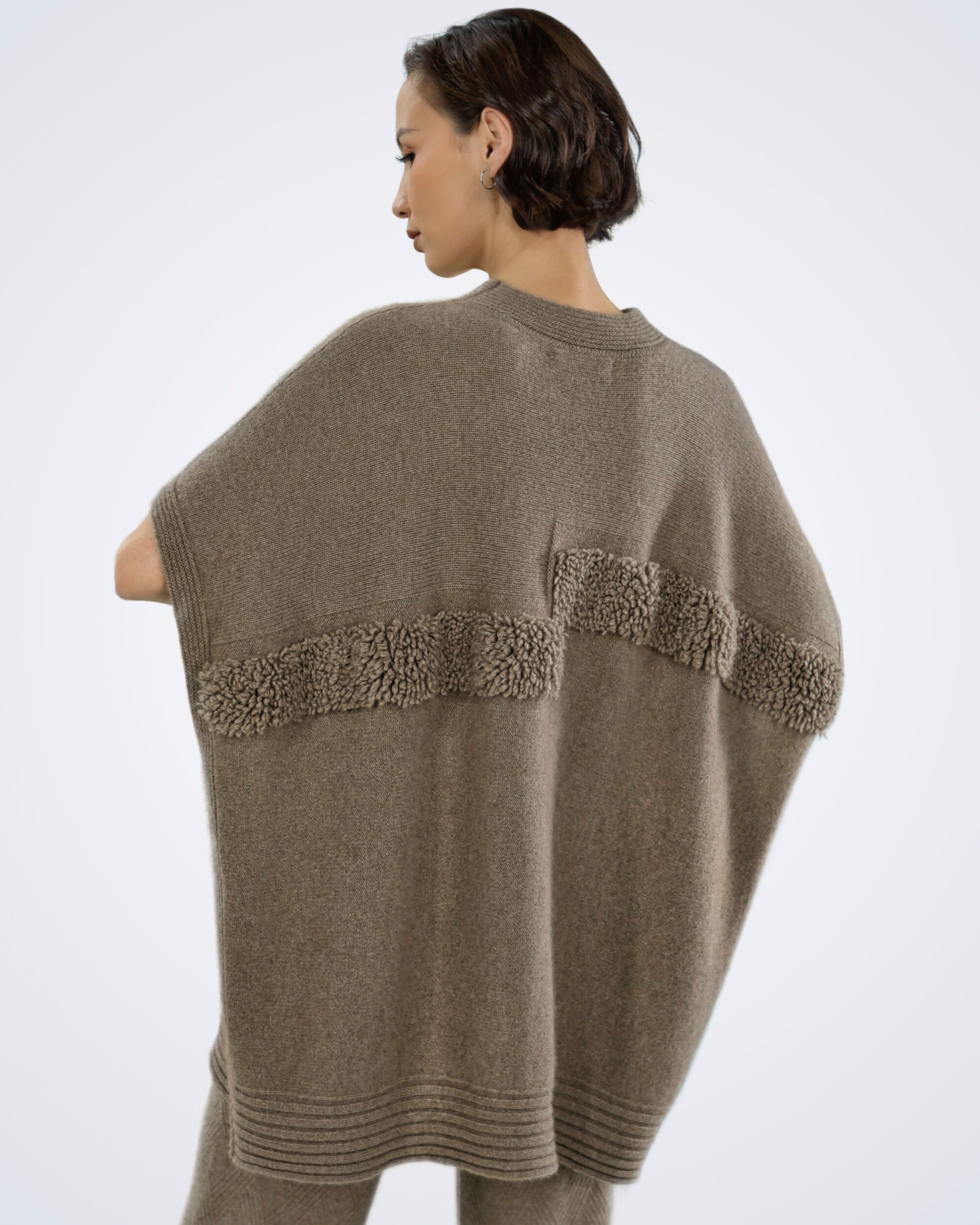 Unur model wearing a natural brown ribbed cashmere poncho with faux fur trim, rear view